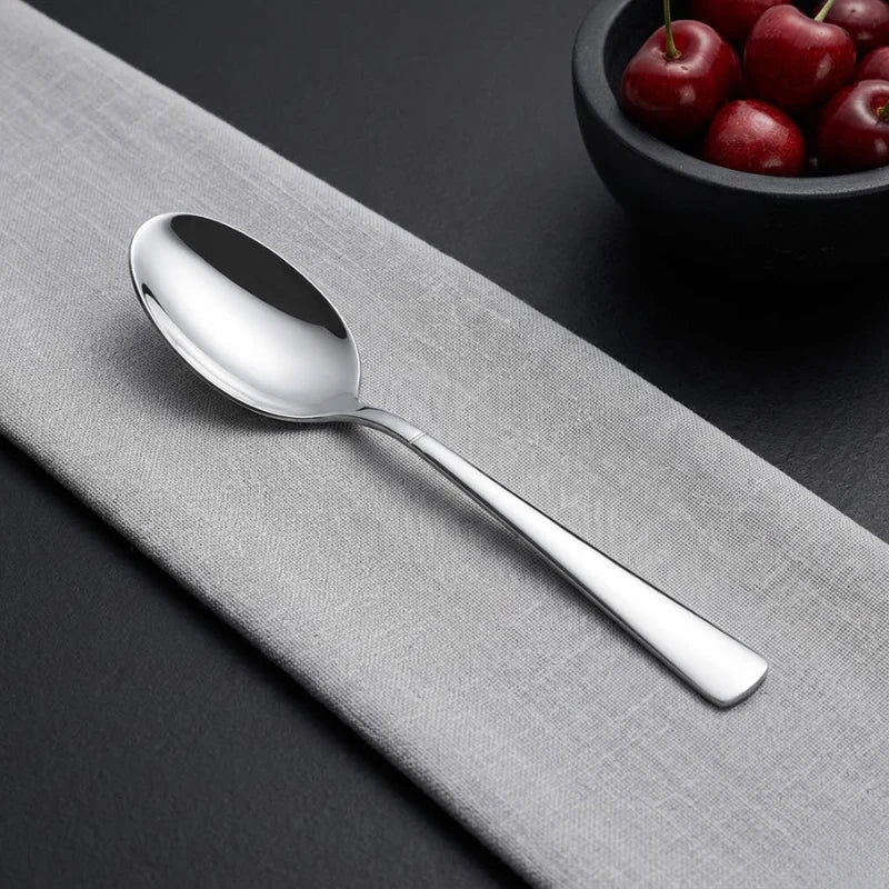 Silver spoon on a gray surface with a bowl of cherries in the background