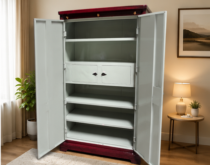 A tall white metal storage cabinet with two doors open, showing multiple shelves and two small front drawers. The cabinet stands in a warmly lit room with curtains, a plant, a side table with a lamp, and framed wall art.