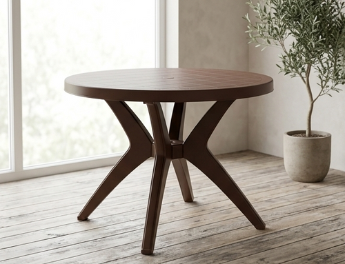 Wooden round table with star-like base in a room with large windows and a plant.