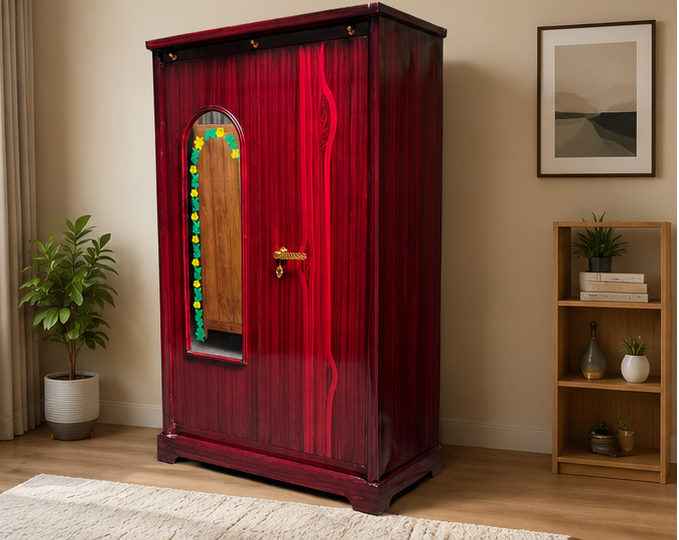 A tall, dark red wooden wardrobe with a glossy finish, featuring an arched mirror on the left door with a colorful floral border and a brass handle. The wardrobe is staged in a room setting with a beige wall, a potted plant on the left, and a wooden bookshelf on the right.