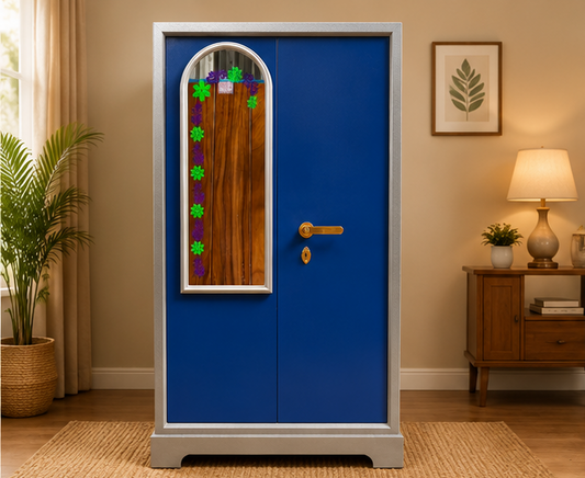 A tall blue door with a silver frame and a decorative arched window panel, shown standing in a styled room with a plant, lamp, and wooden furniture.