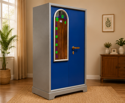 A tall gray and blue wardrobe or cabinet with a decorative arched mirror on the front, shown in a styled room with a window, curtains, a wooden sideboard, and potted plants.