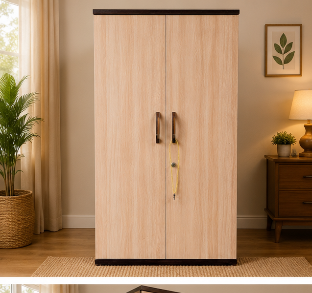 A tall two-door wardrobe or cabinet with a light natural wood grain finish and dark metal handles, shown in a styled bedroom setting with a side table, lamp, framed wall art, and a plant.