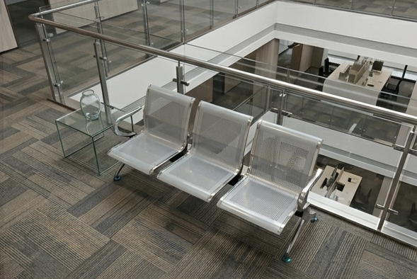 Row of modern metal chairs in a waiting area with glass walls and floor.