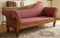 Vintage-style sofa with wooden frame and pink upholstery in a room with books and a clock.