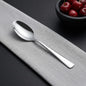 Silver spoon on a gray surface with a bowl of cherries in the background